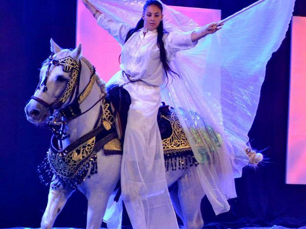 Artiste en costume blanc aux ailes déployées sur un cheval pendant le spectacle du Cabaret Equestre de Camargue, photo réelle du prestataire.
